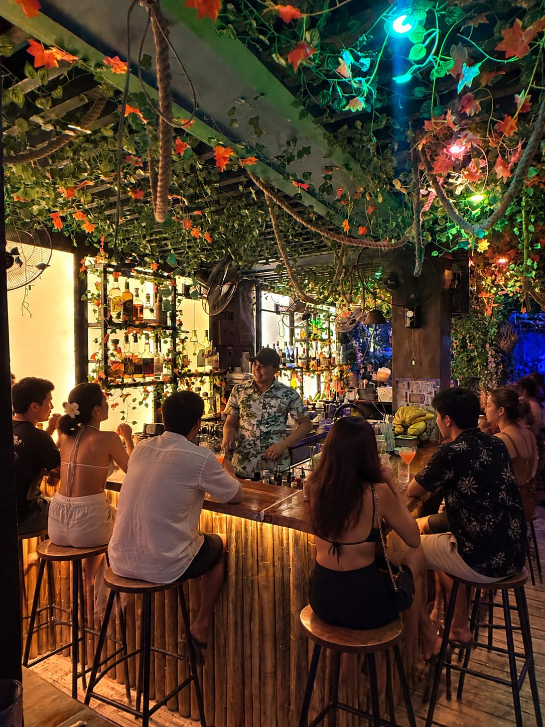 Guests on bamboo bar stools under the lit tiki-jungle canopy at Mai Tai Beach Bar Boracay